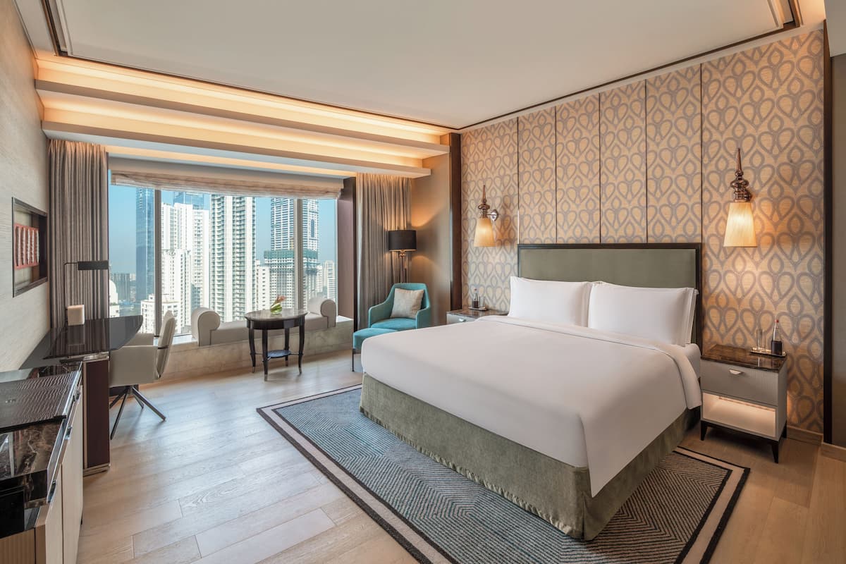 A hotel room with a large bed, a desk, a chair, a small table, and a view of tall buildings.