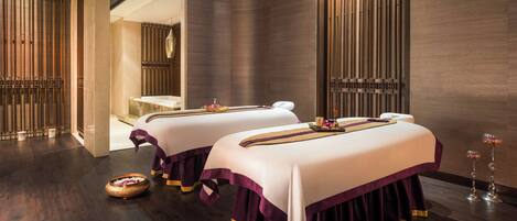 A spa room with two massage tables, dark wooden floors, and decorative elements like flower arrangements.