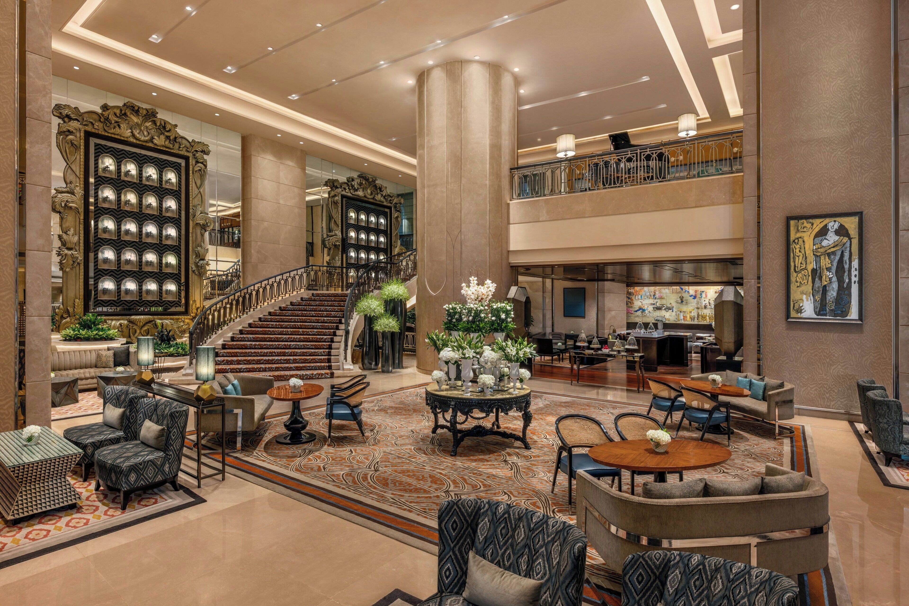 A spacious lobby with a grand staircase, multiple seating areas, and a large decorative wall.