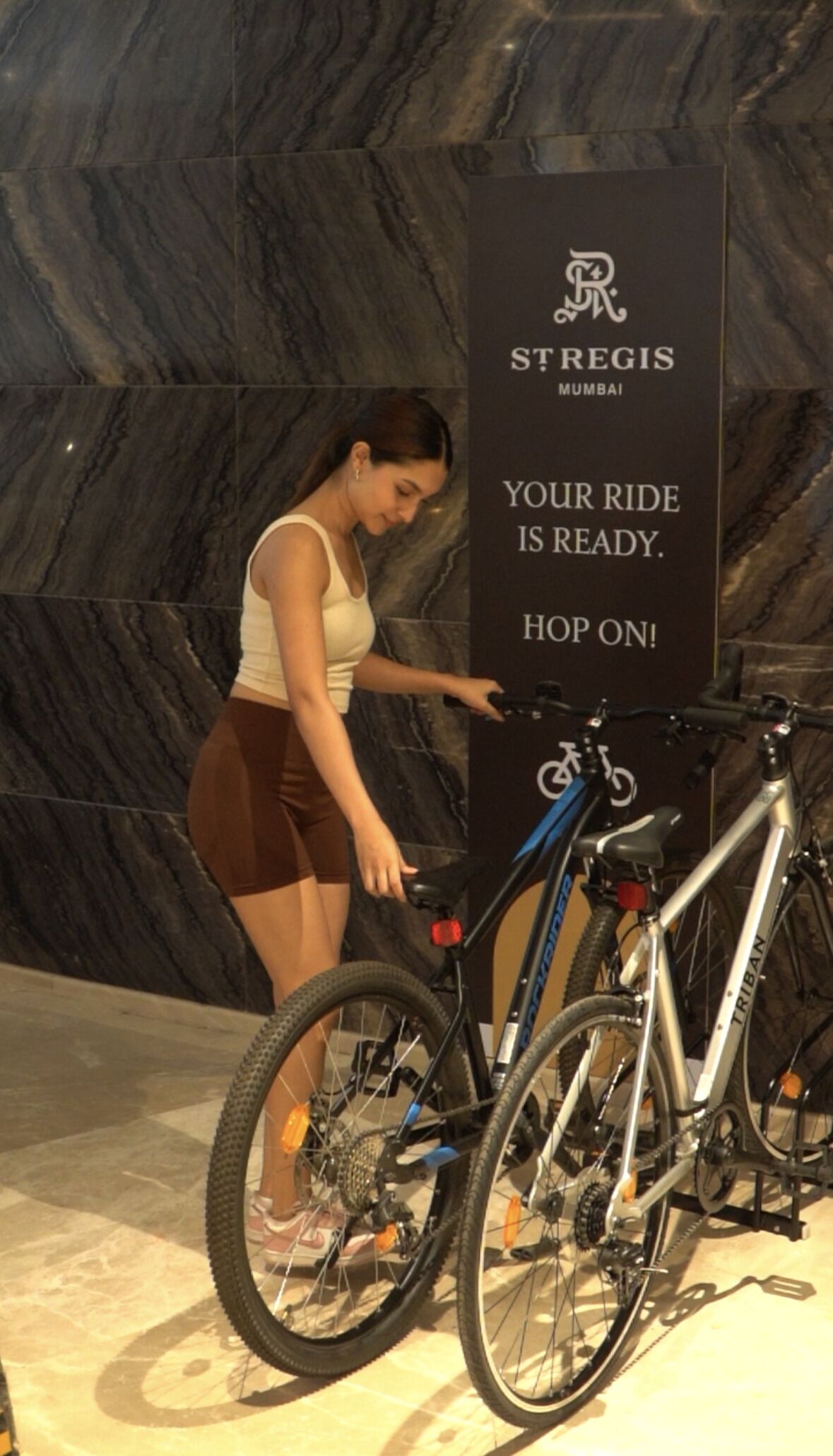 A woman pointing at a sign that says 'Your ride is ready. Hop on!' next to a bicycle.