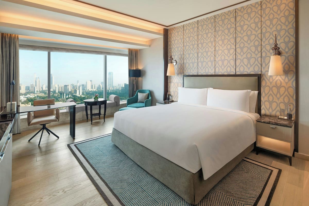 A hotel room with a large bed, a desk, a chair, and a view of a cityscape.