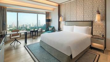 Habitación de hotel con una cama grande, un escritorio, una silla y vistas a un paisaje urbano.