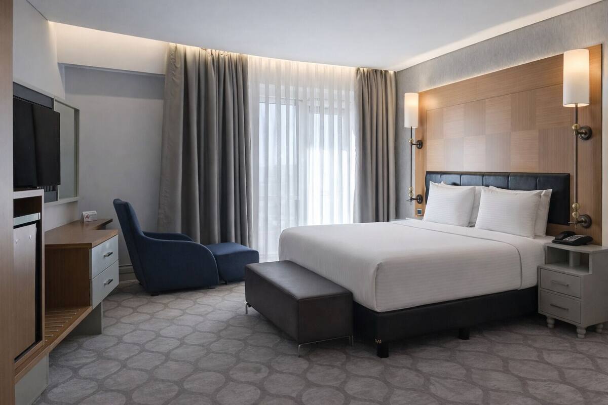 A hotel room with a bed, a desk, a chair, a TV, and a nightstand.