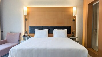 Habitación de hotel con una cama grande, dos mesitas de noche, una silla y un cabecero de madera.