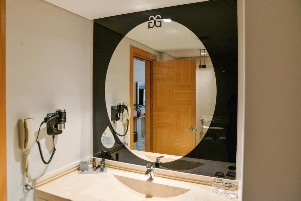 A bathroom with a large mirror, a sink, and a hairdryer mounted on the wall.
