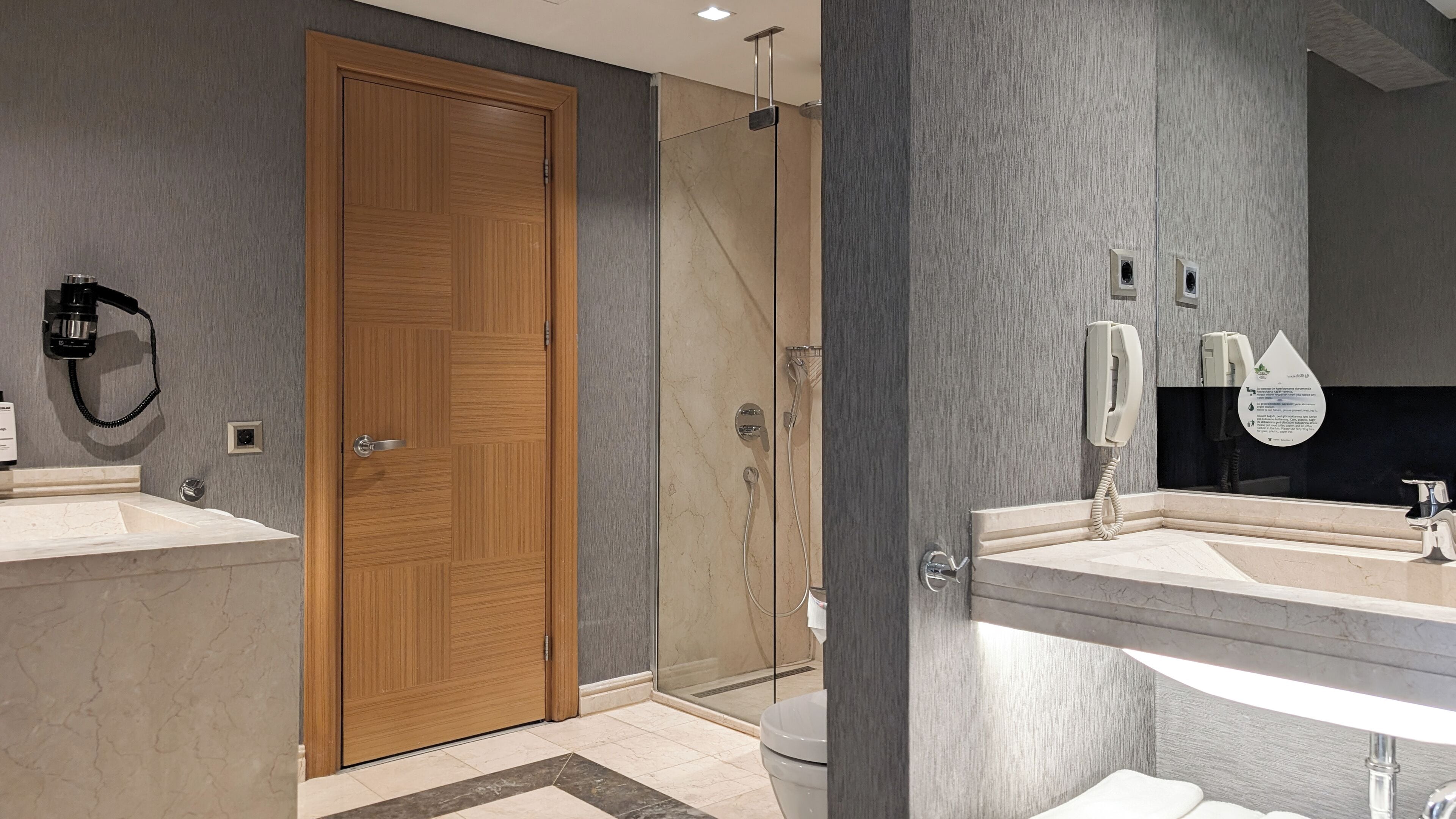 A modern bathroom with a wooden door, a glass shower enclosure, and two sinks with mirrors.