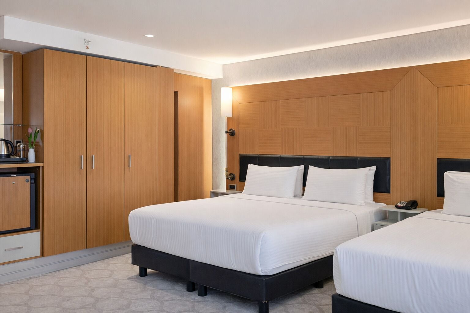 A modern hotel room with two beds, wooden wardrobe, and a small desk with a phone.