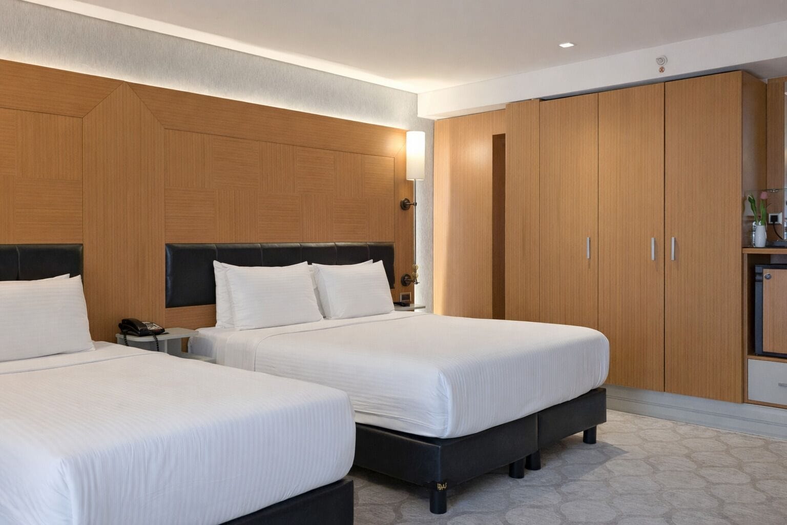 A hotel room with two beds, wooden wardrobe, bedside tables, and a small kitchenette.
