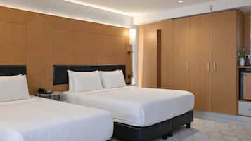 A hotel room with two beds, wooden wardrobe, bedside tables, and a small kitchenette.