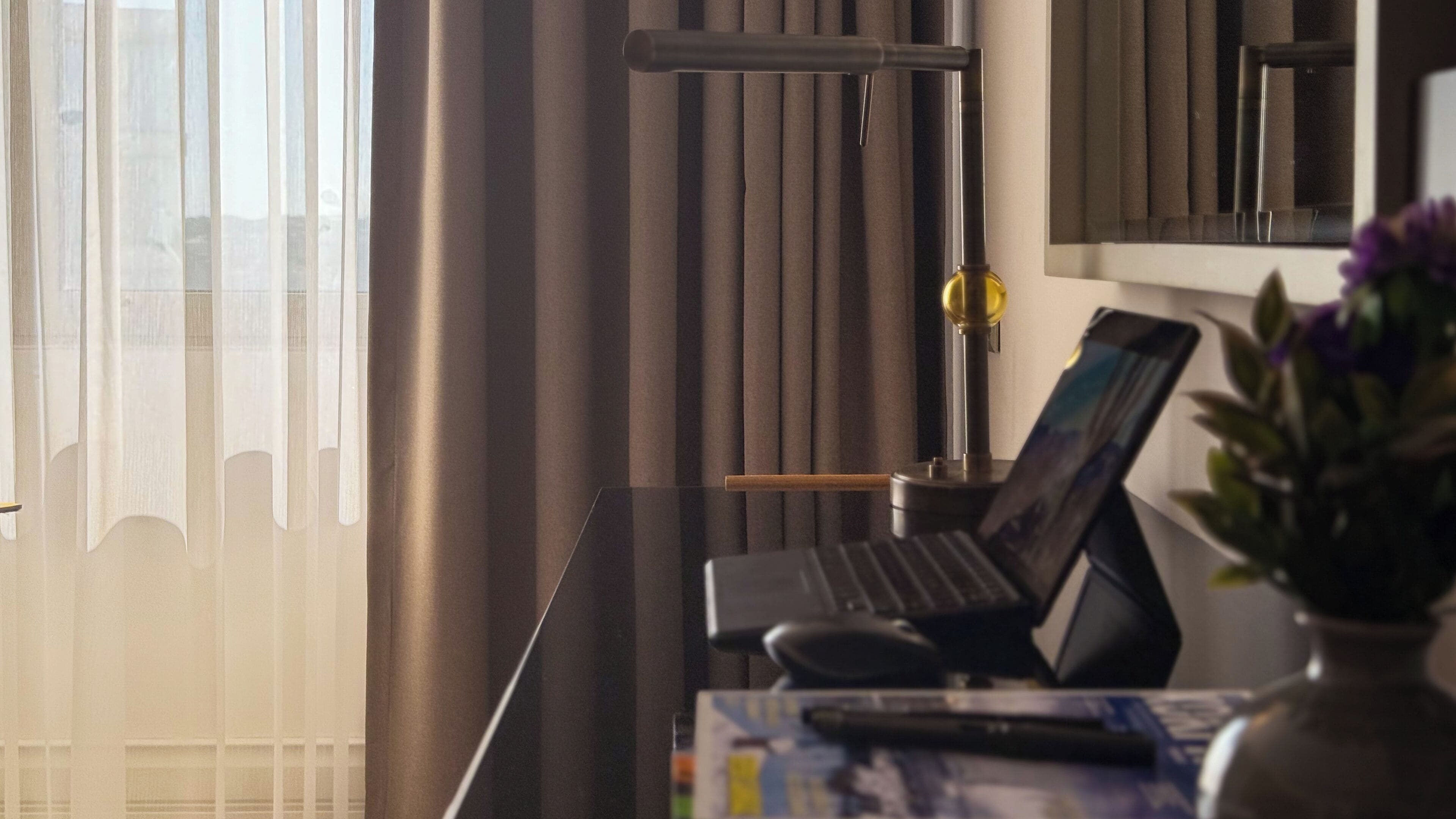 A hotel room with a desk, laptop, and a vase with flowers.