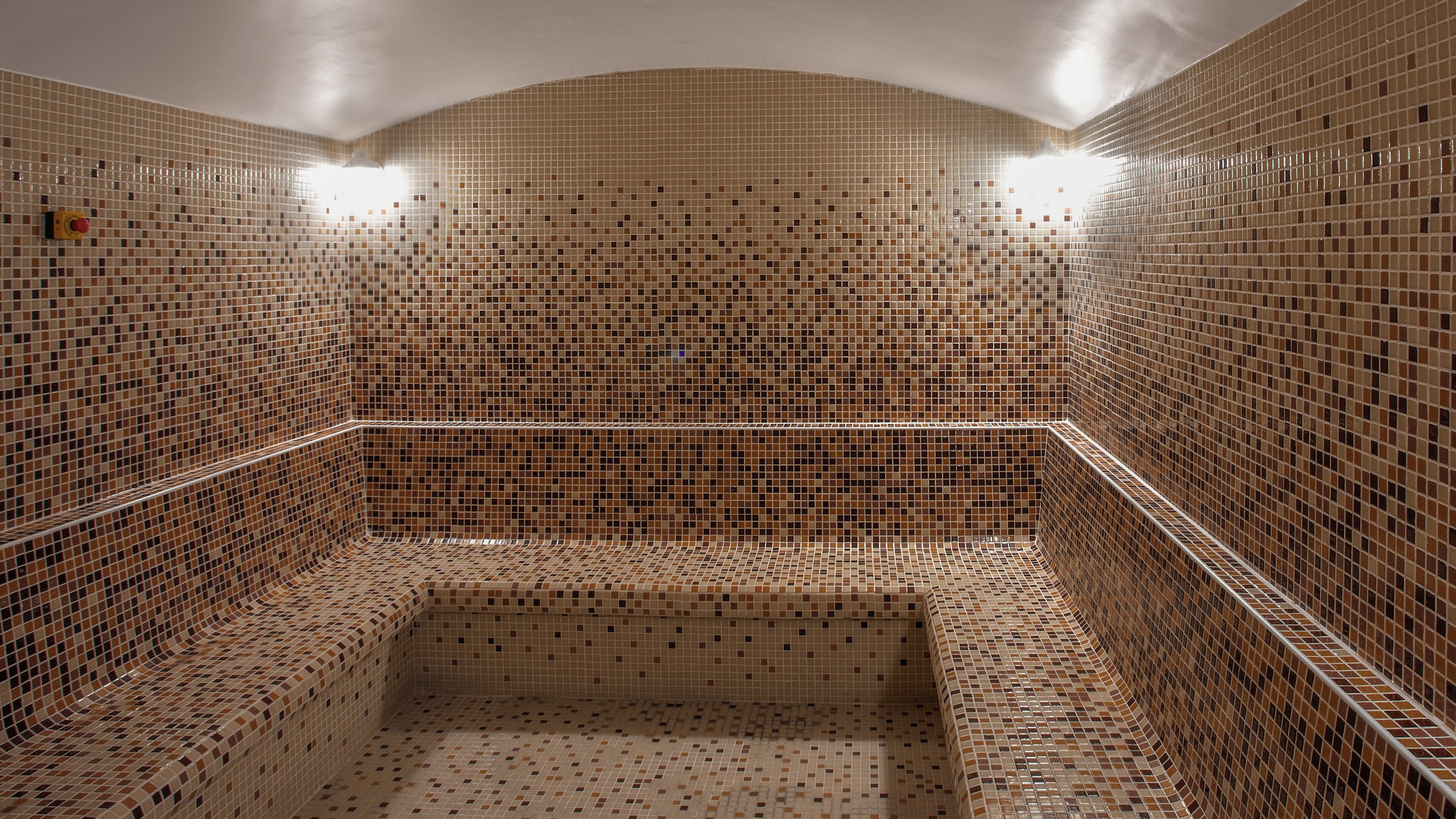 A tiled room with a central square area, likely a shower or bathtub, surrounded by walls and a curved ceiling.