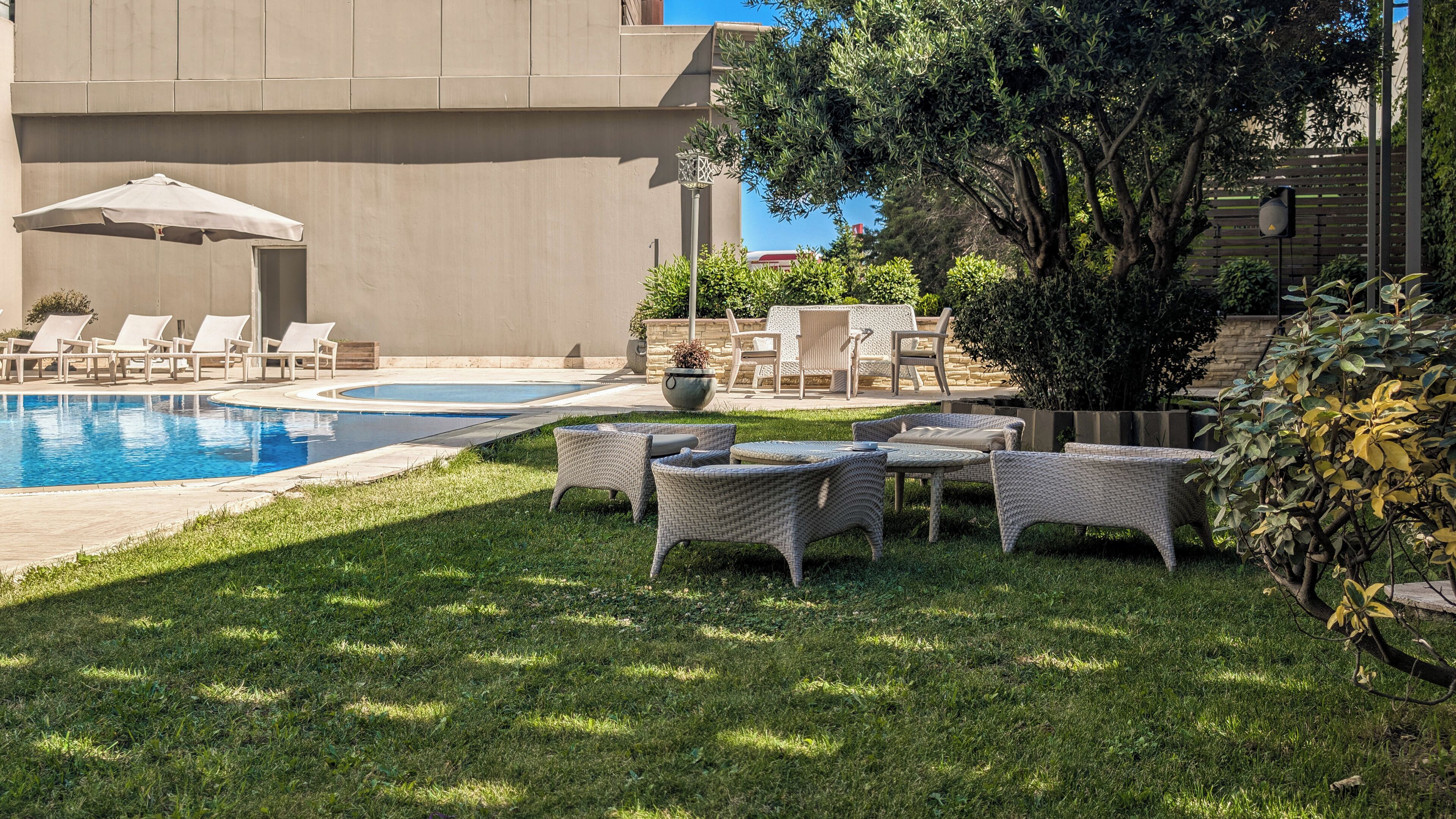 A pool area with lounge chairs and a table, surrounded by grass and trees.