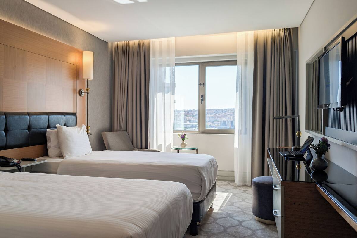 A hotel room with two beds, a desk with a laptop, a phone, and a TV.