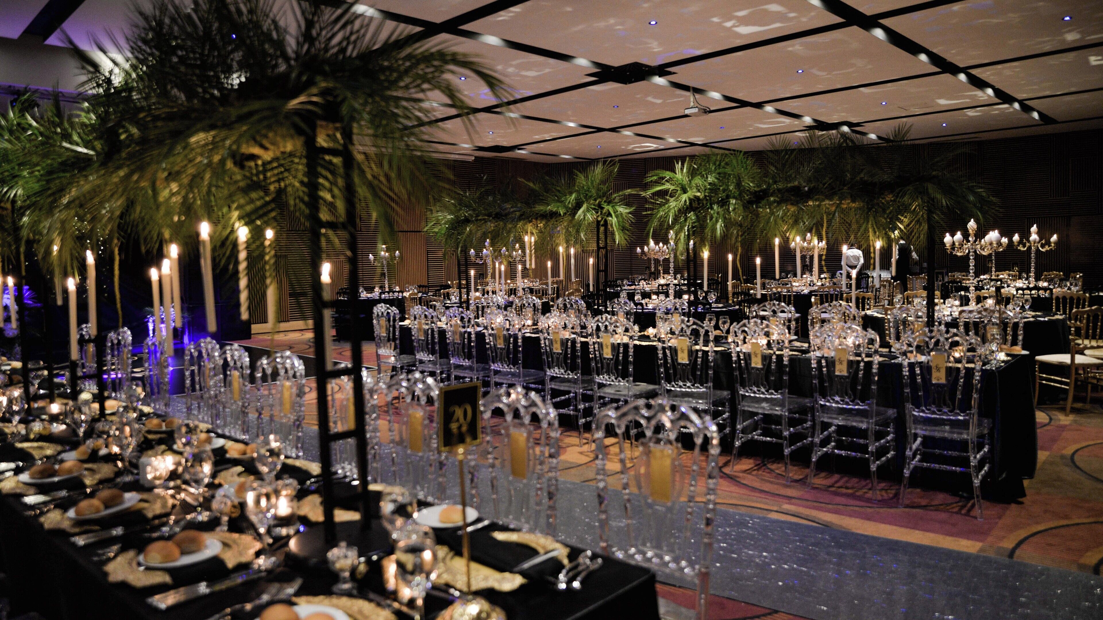 A banquet hall with long tables set for a formal event, featuring crystal chandeliers and candlelit centerpieces.