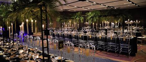 A banquet hall with long tables set for a formal event, featuring crystal chandeliers and candlelit centerpieces.