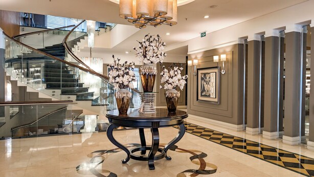 A modern lobby with a glass staircase, a central table with vases, and a check-in desk. - Istanbul Gonen Hotel (Istanbul)