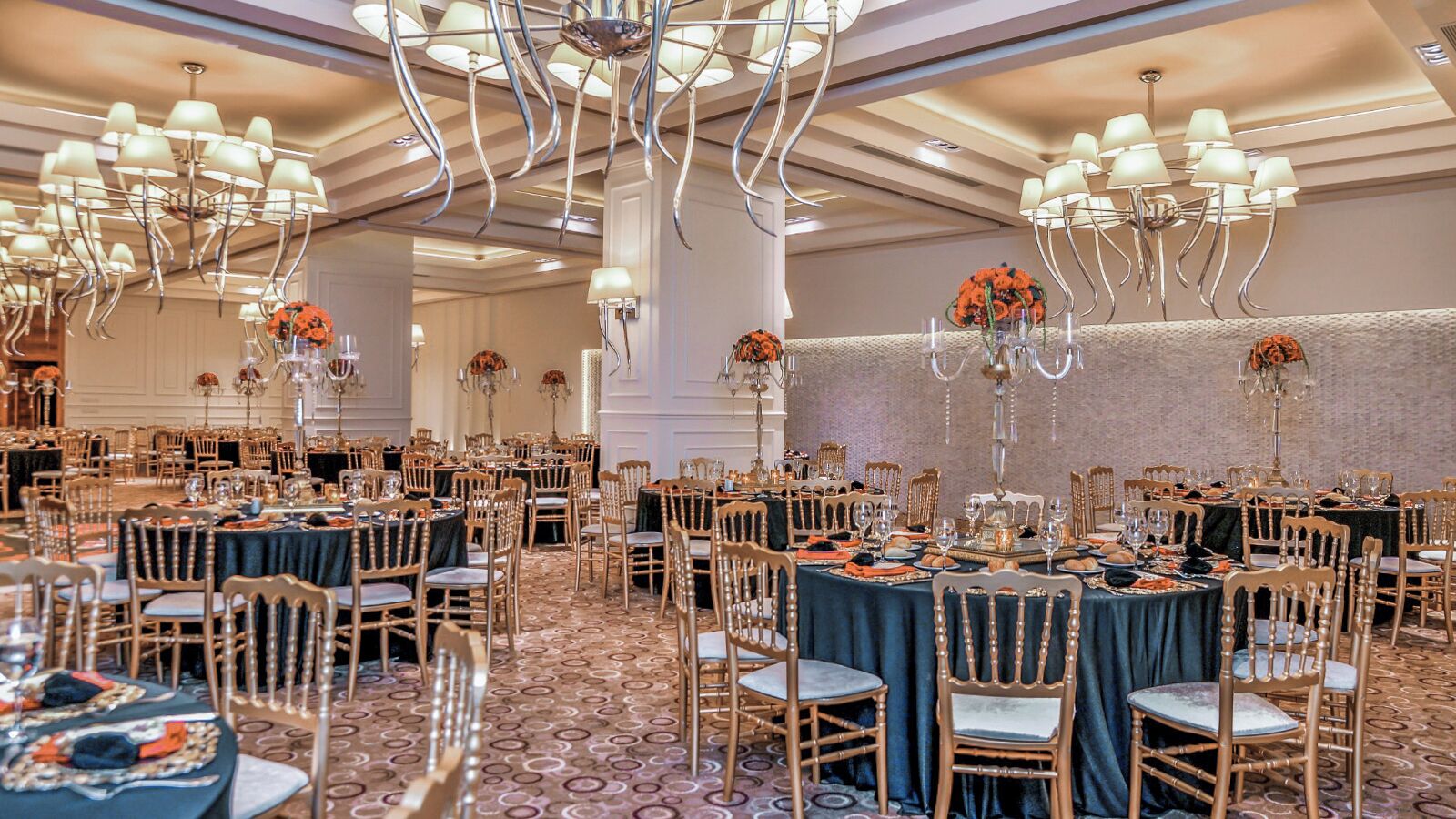 A banquet hall with round tables, chairs, and chandeliers.