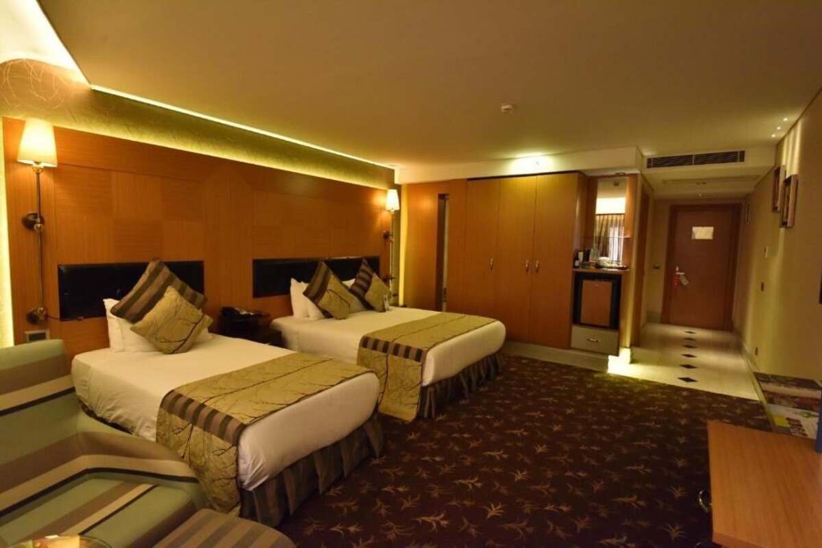A hotel room with two beds, a sofa, a desk, and a small kitchenette.