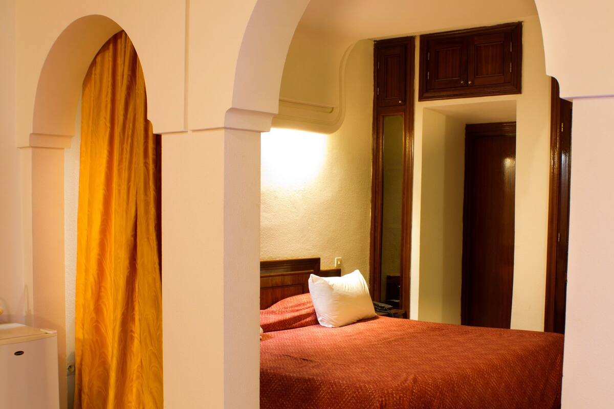 A hotel room with a bed, a nightstand, a lamp, and a wardrobe.
