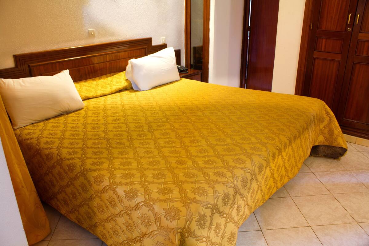 A bed with a patterned bedspread, a wooden headboard, and a nightstand with a lamp.