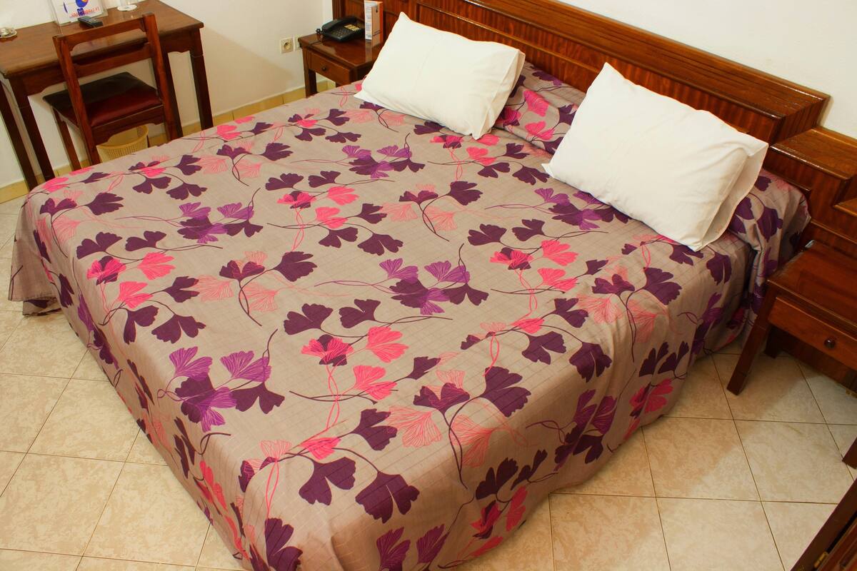 A neatly made bed with a floral bedspread, a wooden headboard, and a bedside table with a lamp.