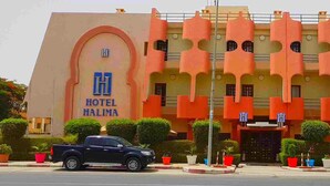Un hôtel à la façade orange distinctive et aux fenêtres en arc, sur lequel on peut lire l’inscription « HÔTEL HALIMA ».