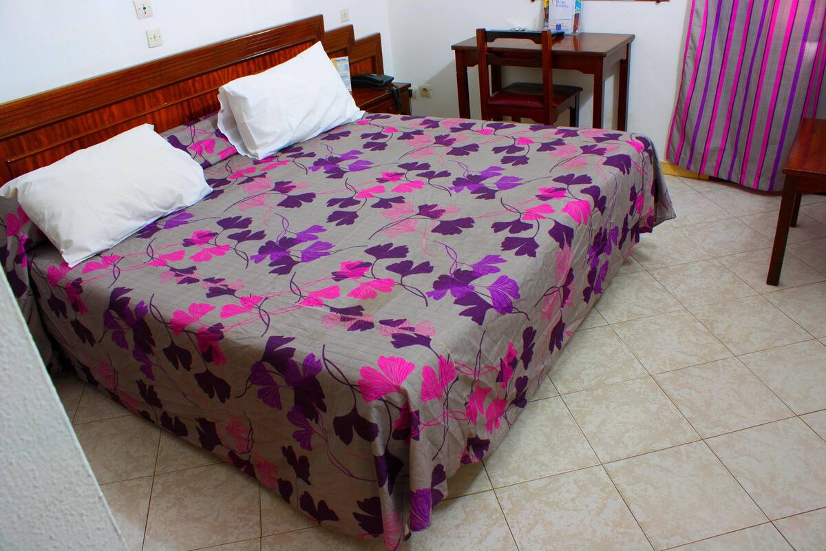 A bed with a floral bedspread, a wooden headboard, and a nightstand with a lamp.