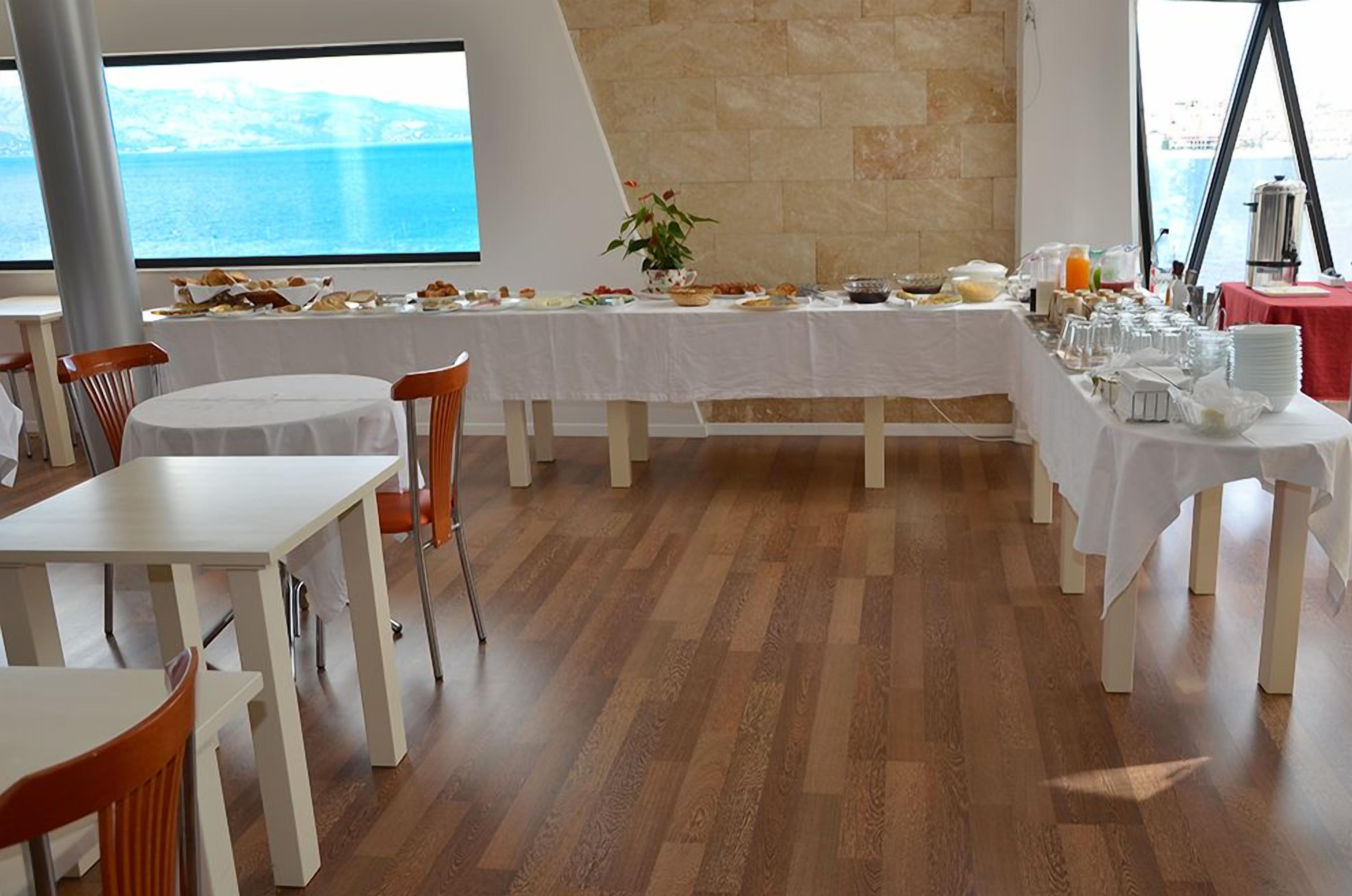 Un comedor con una mesa larga preparada para el desayuno, una planta en maceta y vista al mar.