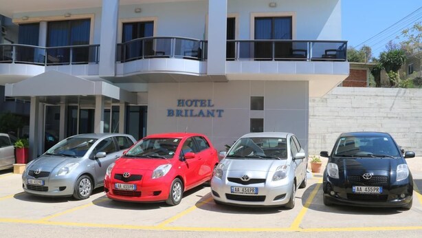 Un hotel llamado 'HOTEL BRILANT' con un estacionamiento que contiene cuatro coches.