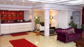 Un hall de hotel con mostrador de recepción, un sofá púrpura y una columna.