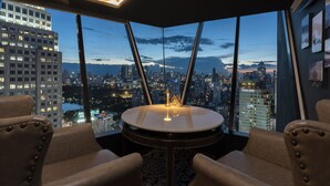A corner room with a round table and two chairs, large windows with a city view, and a ceiling with a map design. - Montraj Continent Sukhumvit Bangkok (Bangkok)