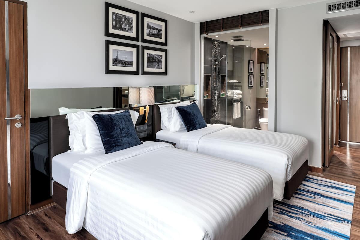 A hotel room with two beds, a large mirror, and a shower area visible through a glass door.