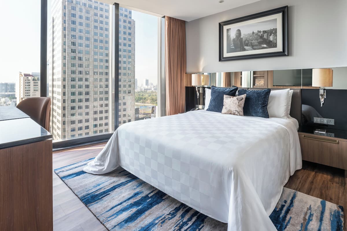 A hotel room with a large bed, a desk, a chair, a city view, and a framed picture on the wall.