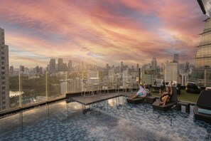 A rooftop pool with a city view, lounge chairs, and a glass barrier. - Montraj Continent Sukhumvit Bangkok (Bangkok)