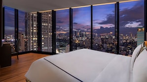 Une chambre d’hôtel moderne, dotée d’un grand lit, d’un bureau et offrant une vue sur le paysage urbain au crépuscule.