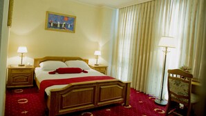 Ein Hotelzimmer mit einem hölzernen Bett, zwei Nachttischen mit Lampen, einem Gemälde an der Wand und einem großen Fenster mit Vorhängen.