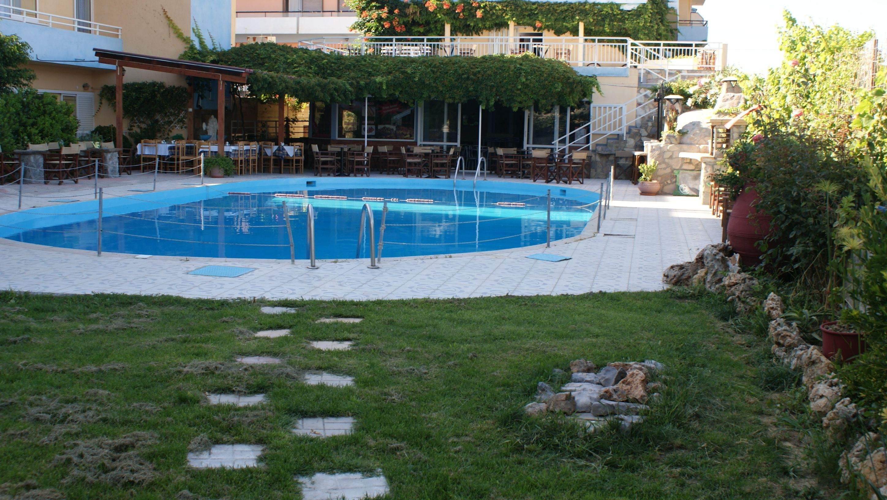 Ein Außenpool, umgeben von einer überdachten Terrasse mit Tischen und Stühlen.