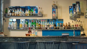 A bar area with multiple shelves of liquor bottles, bar stools, and a blue counter. - Roxani Hotel (Malevizi)