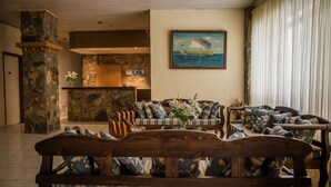 A lobby with a stone pillar, a reception desk, and a seating area with patterned sofas and a wooden bench. - Roxani Hotel (Malevizi)