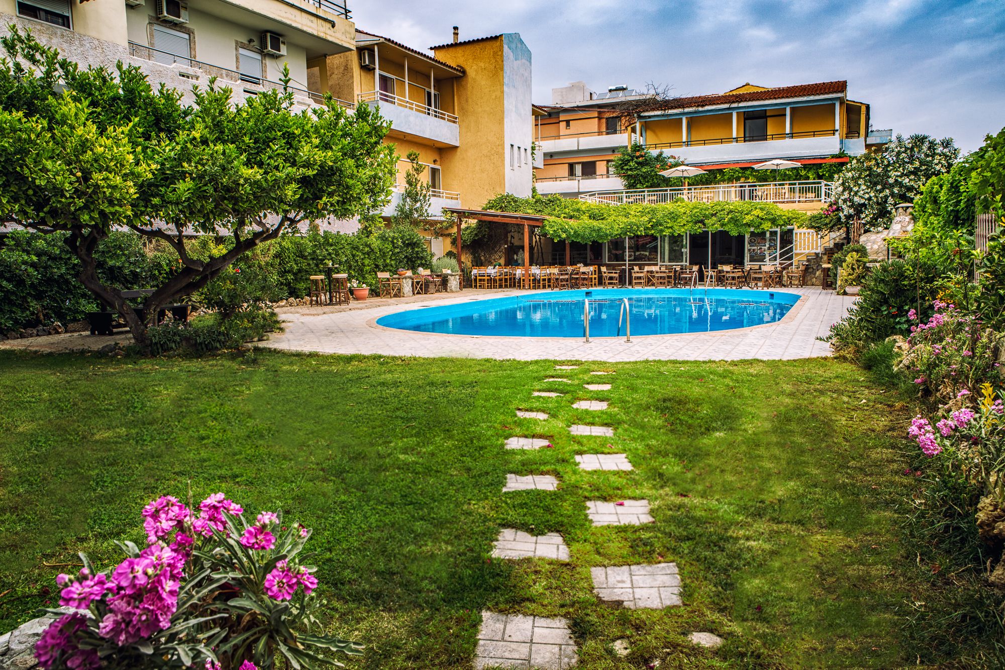 A swimming pool surrounded by a grassy area with stepping stones leading to a patio area with outdoor seating.