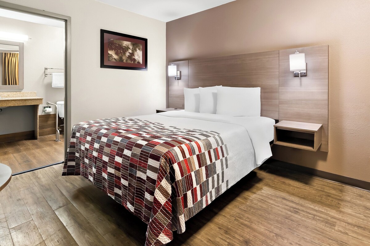 Une chambre d’hôtel avec un grand lit, une tête de lit en bois, une table de chevet, une lampe fixée au mur et un tableau encadré.