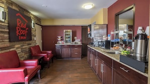 Een hotel lobby met een receptiebalie, een zithoek met rode stoelen en een keuken voorzien van een koelkast en koffiezetapparaat.