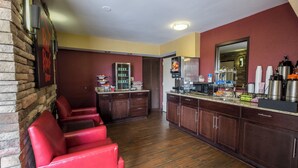 A kitchen with wooden cabinets, a refrigerator, and a microwave. There are red chairs and a counter with various items. - Red Roof Inn Rock Hill (Rock Hill)