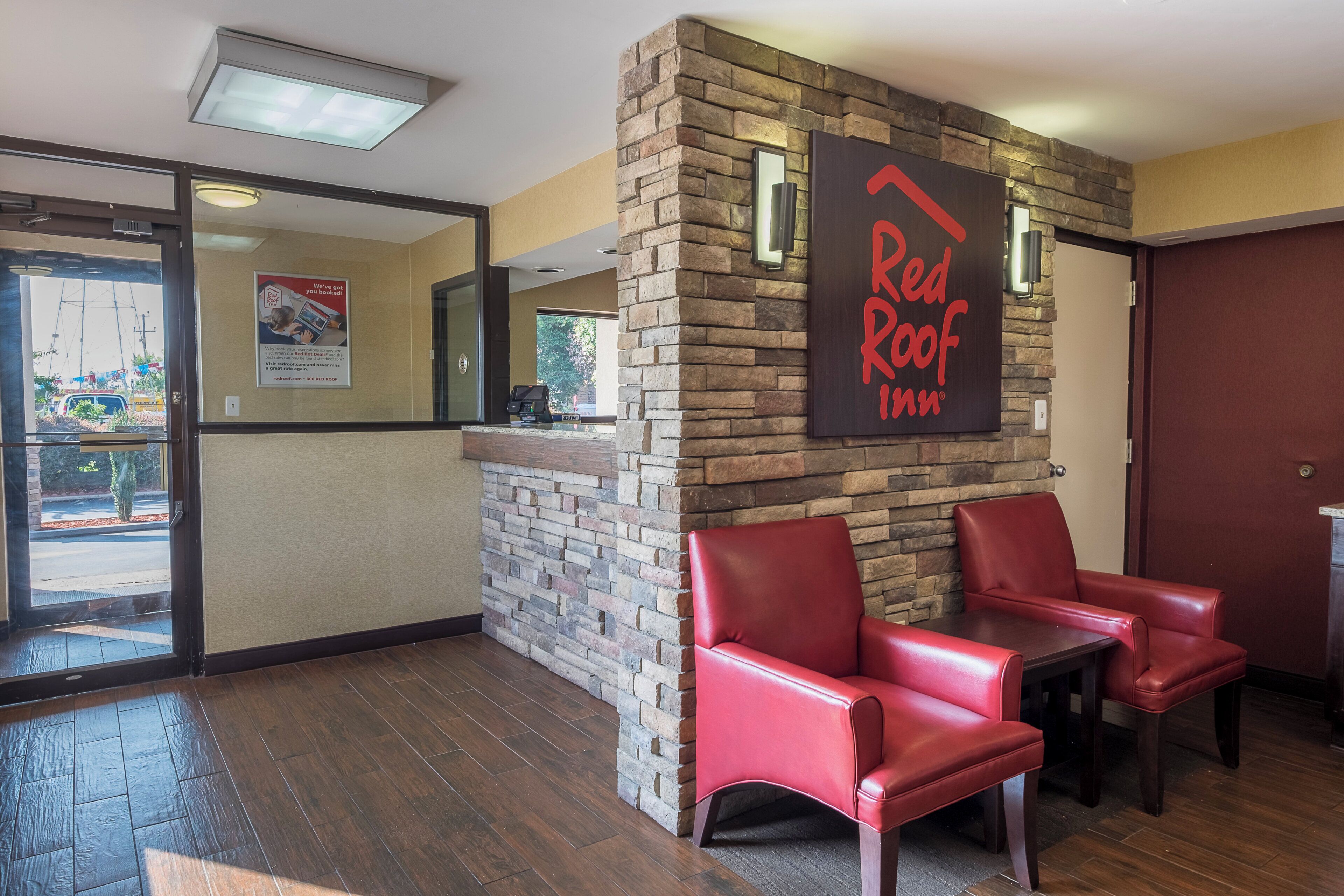 Vestíbulo de Red Roof Inn con una pared de piedra, dos sillones de cuero rojo y un mostrador de recepción de madera.