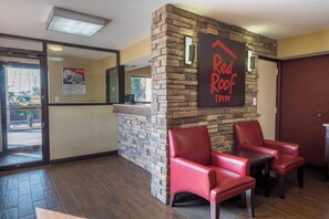 Vestíbulo de Red Roof Inn con una pared de piedra, dos sillones de cuero rojo y un mostrador de recepción de madera.
