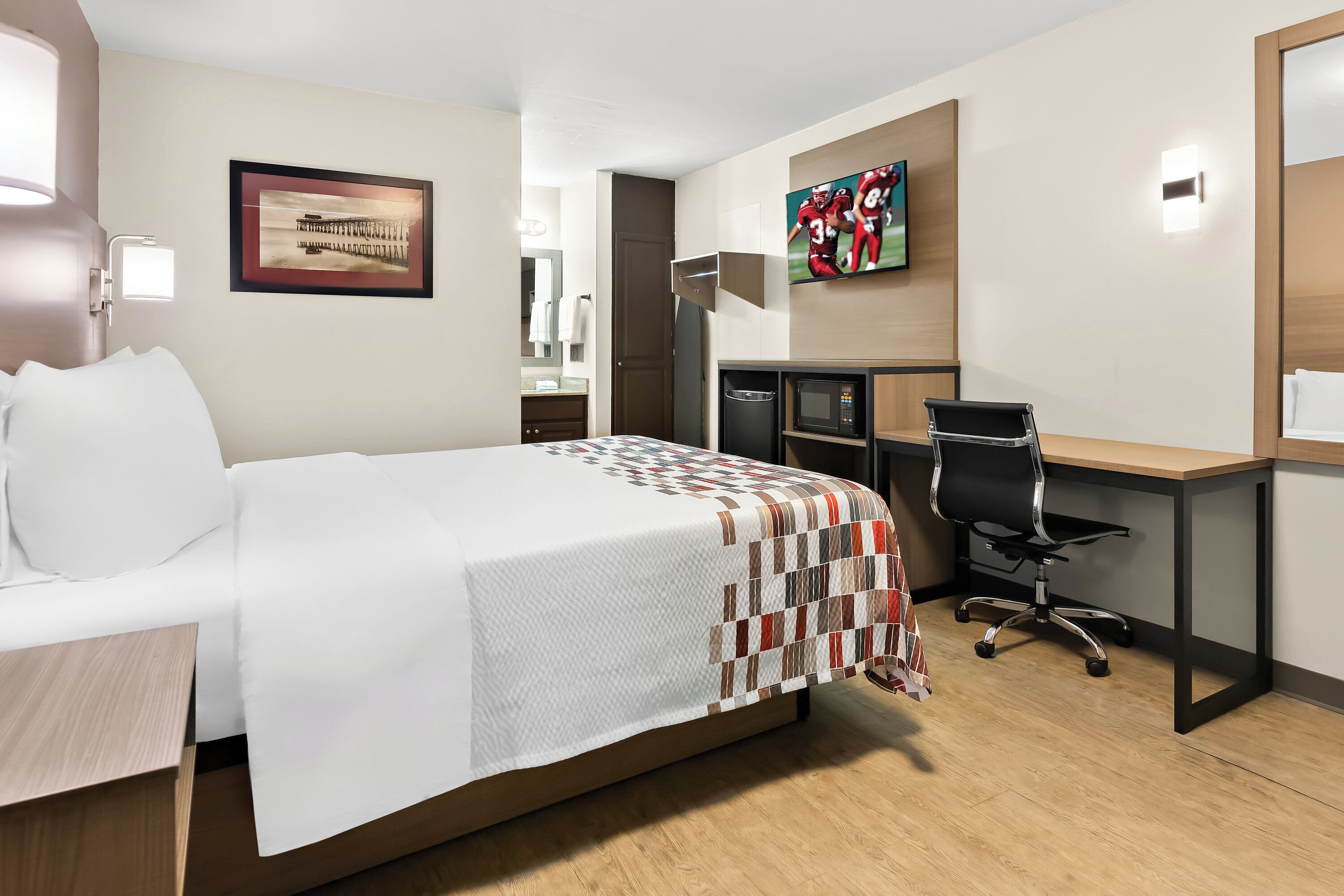A hotel room with a bed, a desk, a chair, a TV, and a microwave.