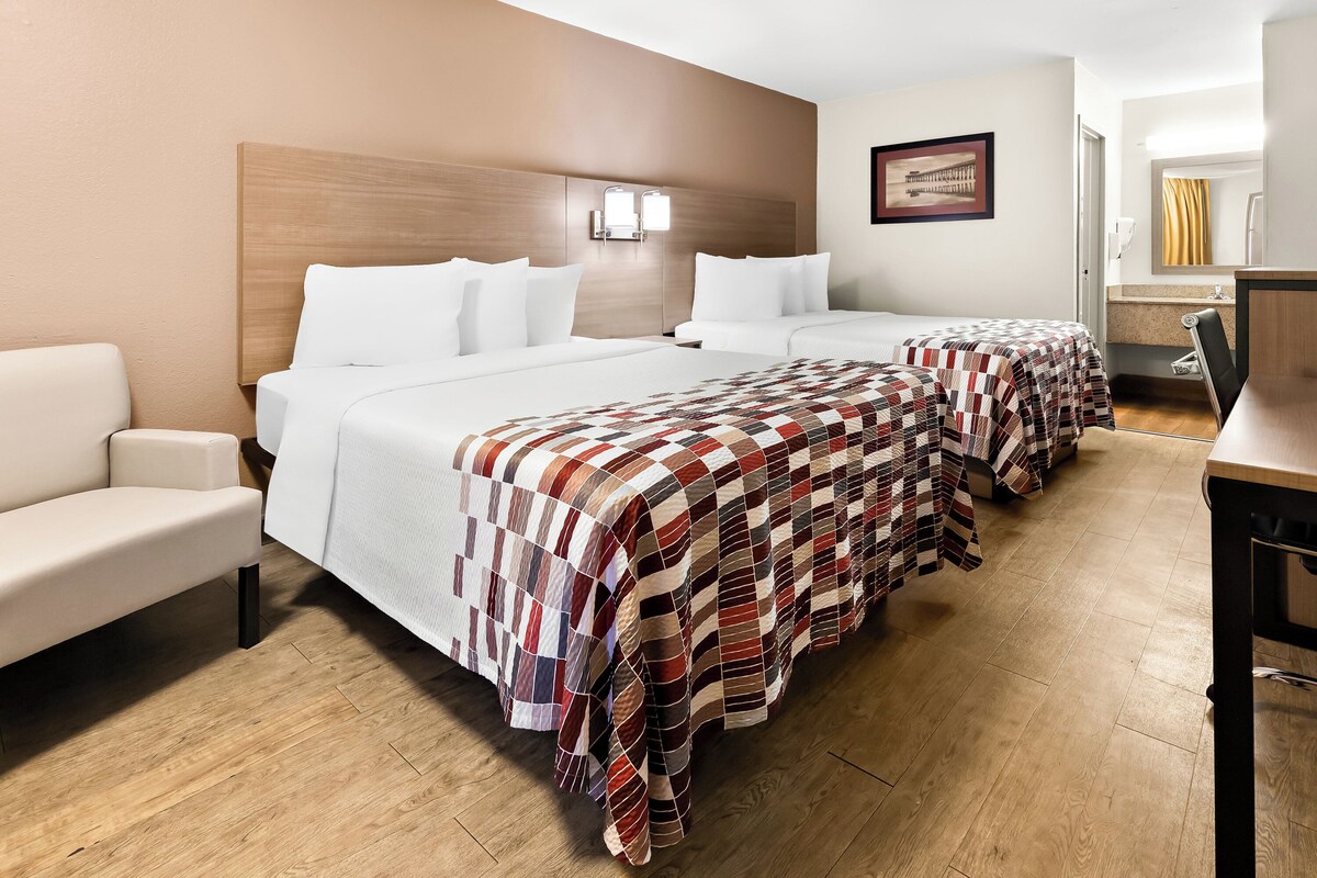 A hotel room with two beds, a sofa, a desk, and a bathroom with a mirror and sink.
