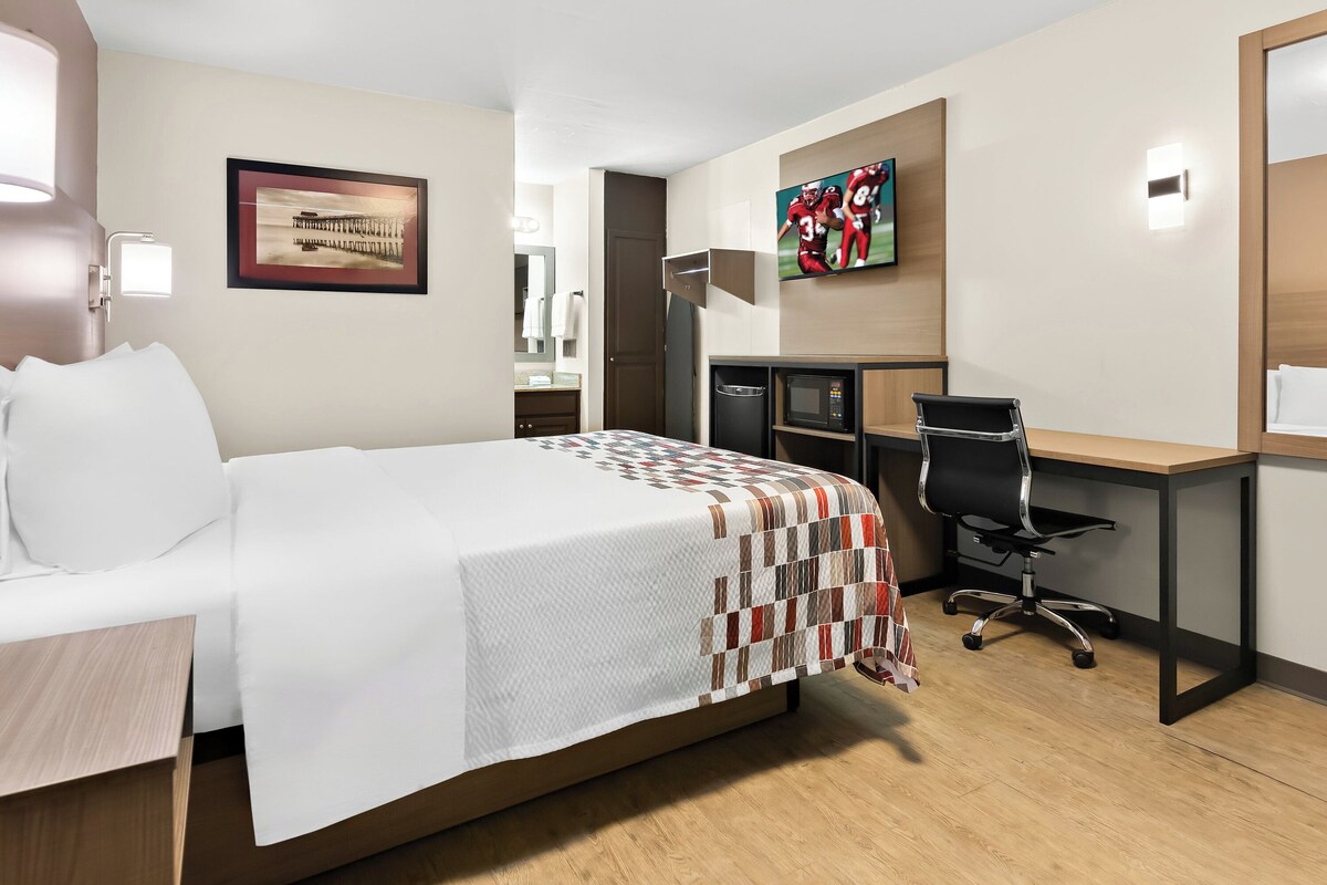 A hotel room with a bed, a desk, a chair, a TV, and a microwave.
