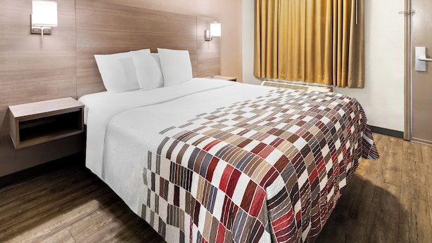 A hotel room with a large bed, wooden headboard, bedside tables, a quilted bedspread, and a window with curtains. - Red Roof Inn Rock Hill (Rock Hill)