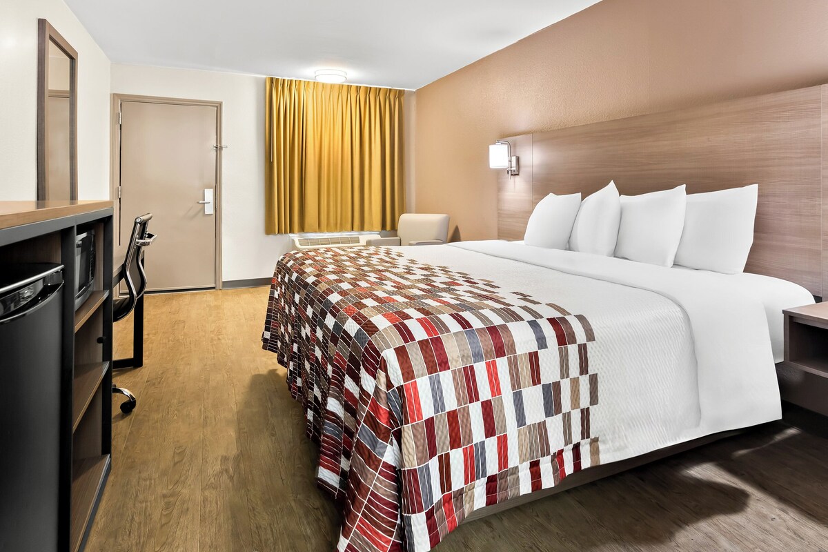 A hotel room with a large bed, a desk, a chair, and a wardrobe.